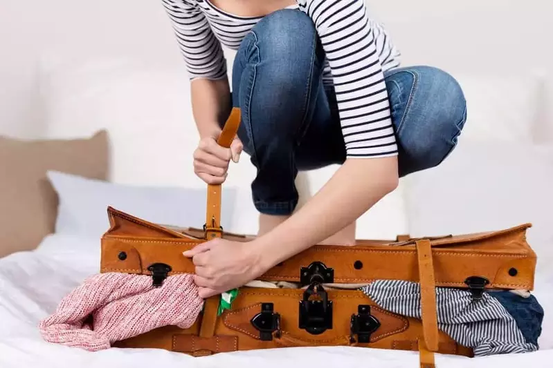 woman trying to close suitcase overflowing with clothes