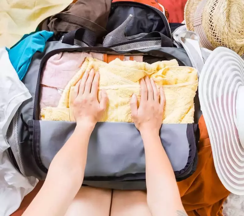 Hands packing a suitcase full of clothes