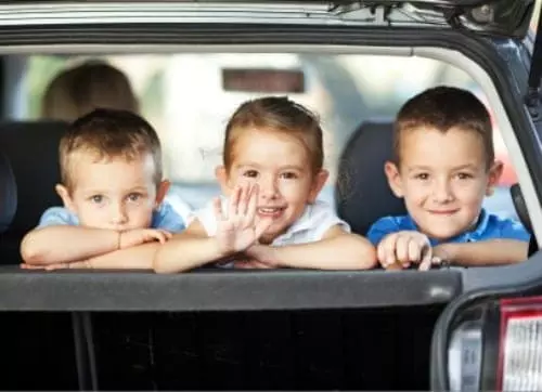 Three children waving from the back of a car