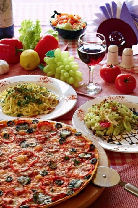 a table with pizza pasta and wine on red checked tablecloth