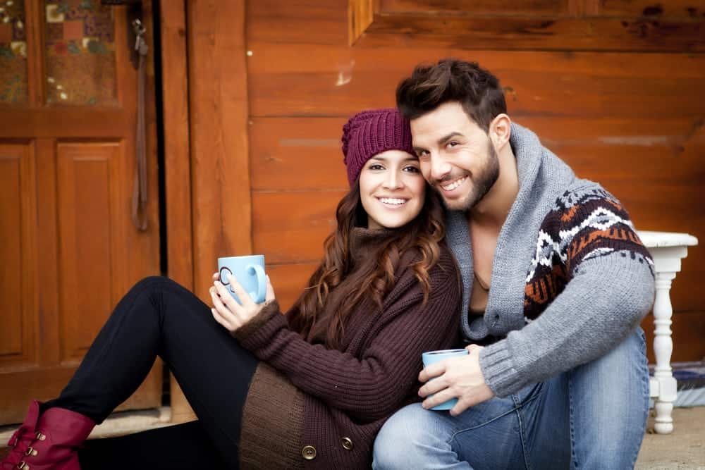 Young couple smiling and drinking cocoa on the deck of a cabin
