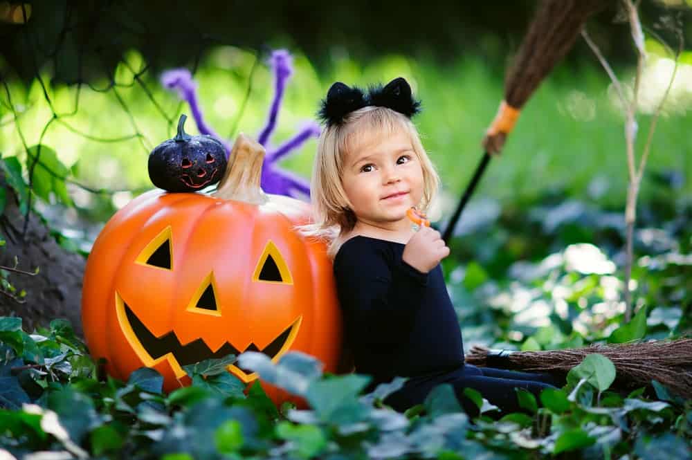 little girl dressed as black cat with pumpkin on Halloween