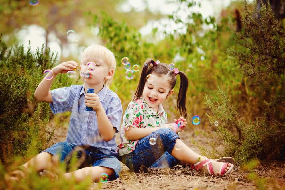 two children sitting in the grass blowing bubbles