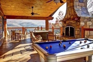 a pool table and stone fireplace on the deck of a Gatlinburg cabin with mountain view
