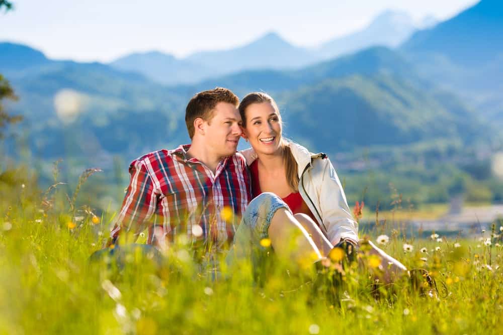 a couple sitting in a field of flowers with mountains in background